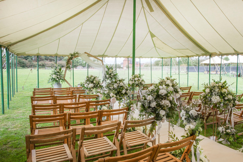 Outdoor wedding ceremony in vintage marquee with wood folding chairs and white floral